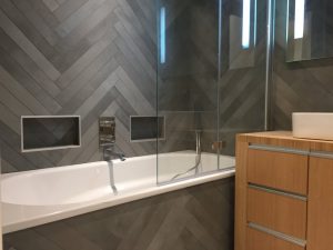 Salle de bains carrelage chevrons gris avec niches et baignoire